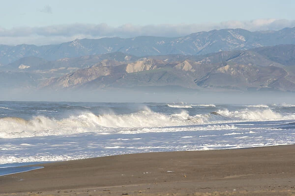US, CA, Oxnard. Offshore wind blows spray back from waves. Ventura and foothills