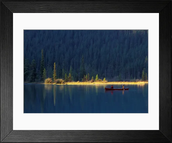 Framed Print : Two people paddle in a canoe in the early morning light, with lush forest behind them Framed Print : Two people paddle in a canoe in the early morning light, with lush forest behind them