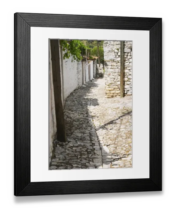 Framed Print : A narrow cobble stone street lined with white stone houses. Berat upper citadel old walled city