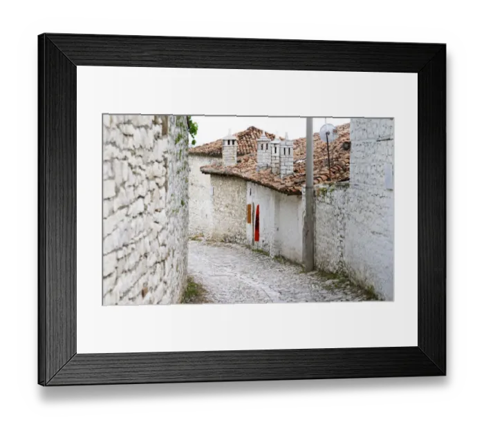 Framed Print : Cobble stone street with traditional ottoman white stone houses. An Albanian flag on the wall