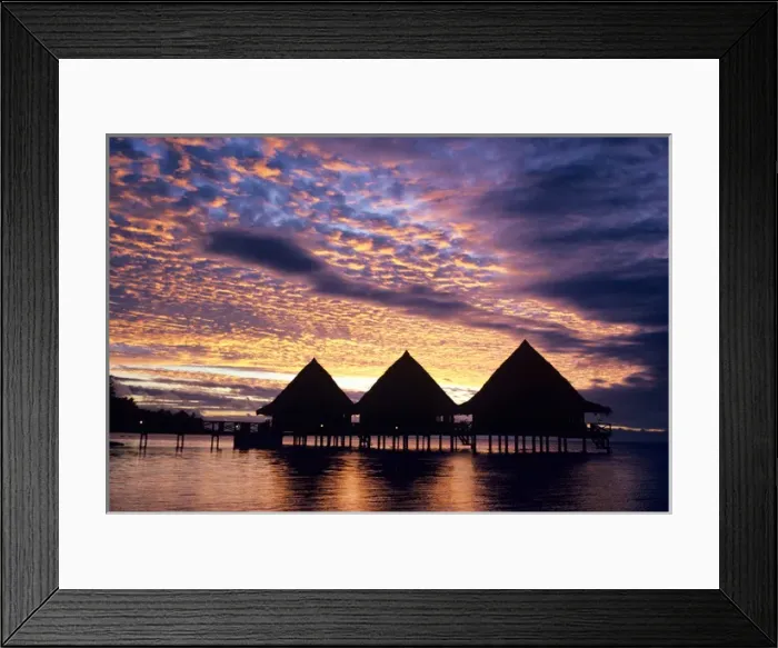 Framed Print : A spectacular sunset silhouettes a group of thatched-roof overwater bungalows in
