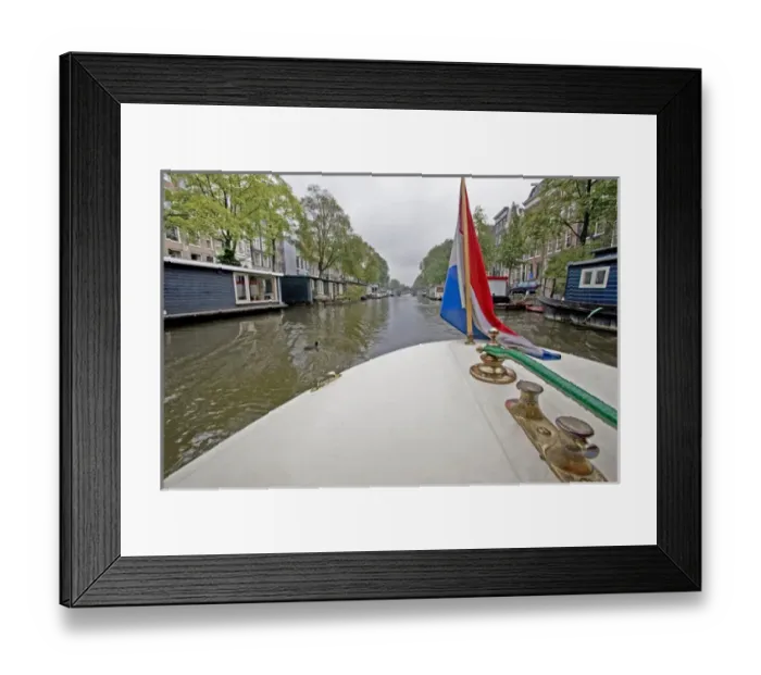 Framed Print : View from the front of a boat with a colorful flag, traveling a canal lined with