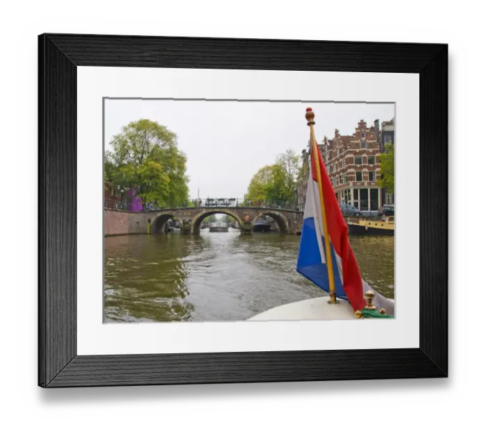 Framed Print : View from the front of a boat with a colorful flag, traveling a canal towards a bridge