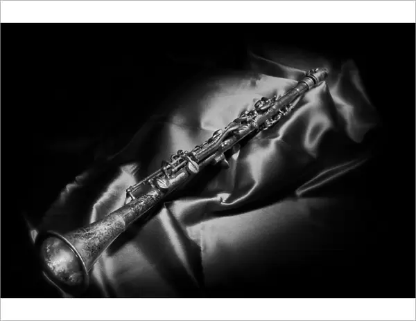 A black and white still life image of a brass clarinet