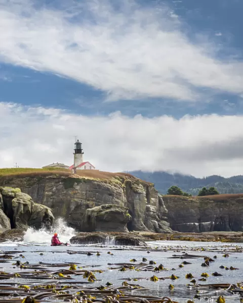 USA, Washington State, Male sea kayaker paddling along cliffs beneath lighthouse