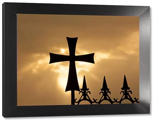 A wrought-iron cross on a fence in Syria at sunrise