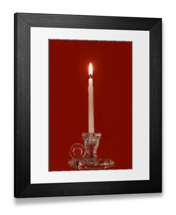 Framed Print : Burning candle in a glass candle holder on red background