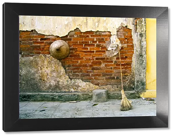 Still-life of a hat and broom against a weathered wall in Vietnam