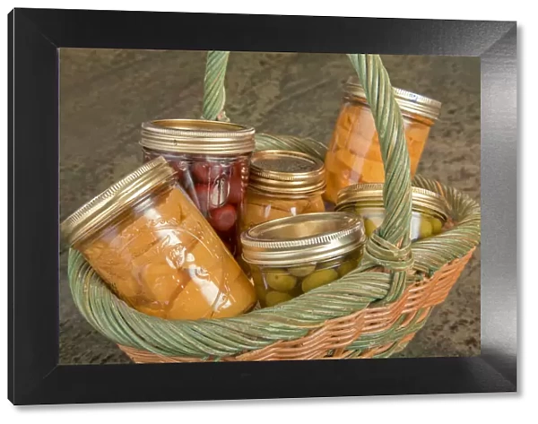 Wicker basket of home canned foods (peaches, olives and cherries) on a granite countertop