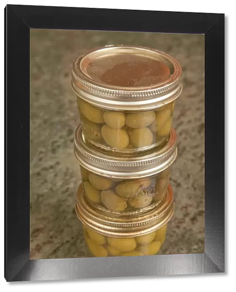 Three jars of home canned olives on a granite countertop in a kitchen