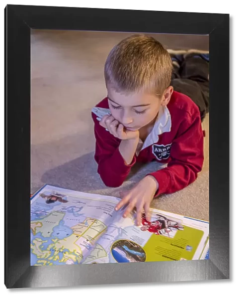 Seven year old boy reading his world atlas book. (MR)
