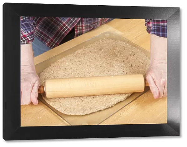 Woman rolling ball of bread dough with a rolling pin to flatten it, prior to forming