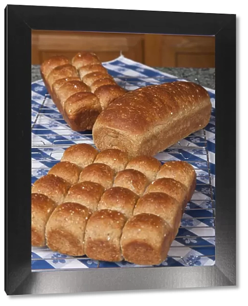 Multigrain rolls and loaf on cooling rack on counter covered by tea towel