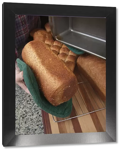 Woman removing loaf of just baked multigrain bread from bread pan. (MR)