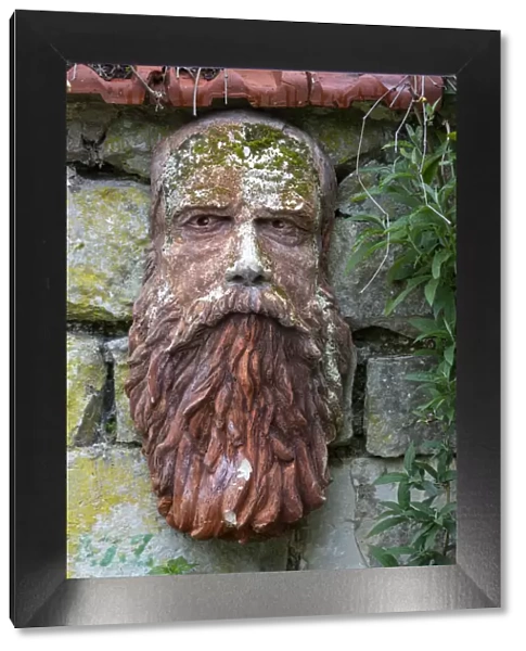 France, Giverny. Stone face hanging on a stone wall. Credit as