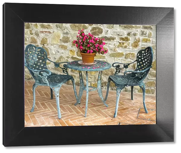 Europe, Italy, Chianti. Table and chairs with a flowering begonia in the center against a