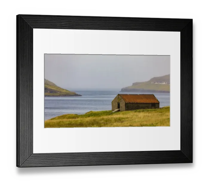 Framed Print : Europe, Faroe Islands. View of sheep shelter on a grassy meadow overlooking the village