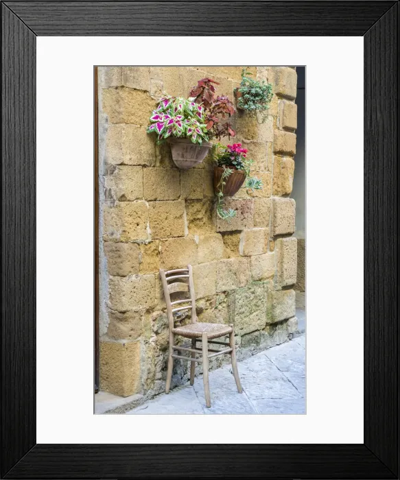 Framed Print : Italy, Tuscany. Chair and flower pots outside the entrance to a shop in a village in Framed Print : Italy, Tuscany. Chair and flower pots outside the entrance to a shop in a village in