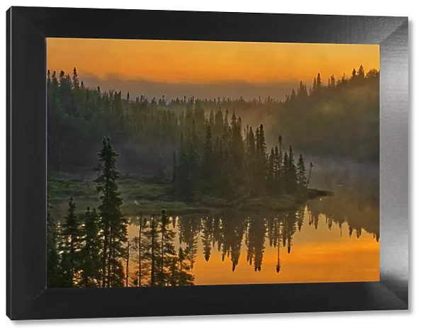 Canada, Ontario, Schreiber. Sunrise fog and forest reflect in lake