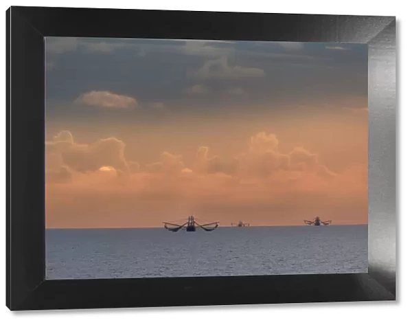 Fishing boats deep out to sea against the backdrop of dramatic sunset clouds and sky