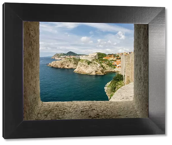 Croatia, Dubrovnik. Ancient fortress on the cliff edge of Dubrovnik protects the port as seen from through a window on the wall surrounding the city