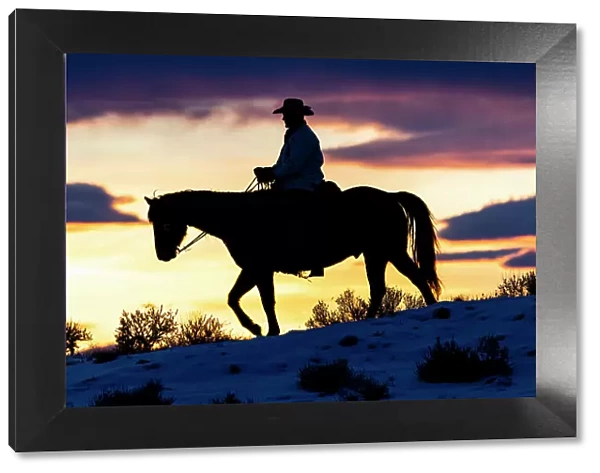 USA, Shell, Wyoming. Hideout Ranch cowboy on horseback silhouetted at sunset. (PR, MR)