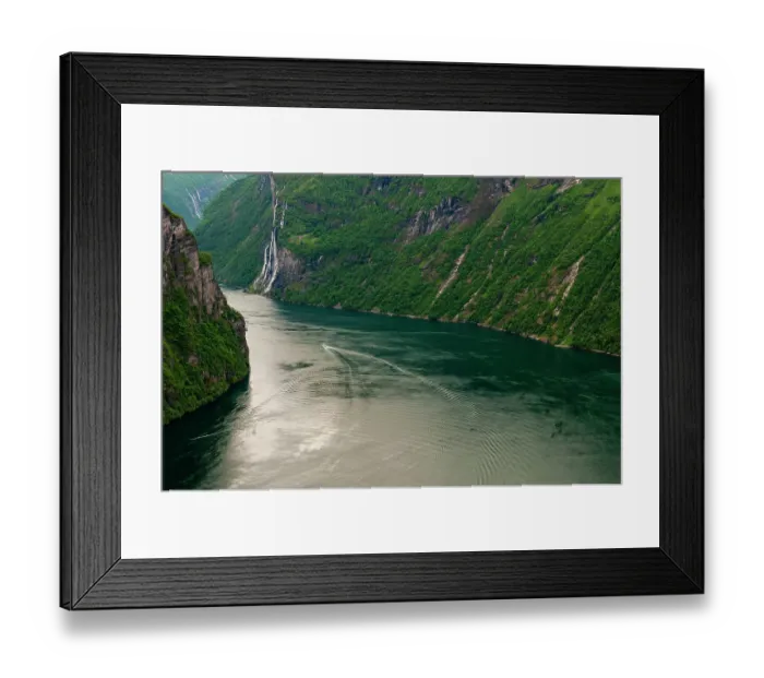 Framed Print : A boat's wake ripples Geirangerfjord as it winds through forest covered sheer cliffs and mountains, Seven Sisters waterfalls is in the distance. Geirangerfjord, Norway