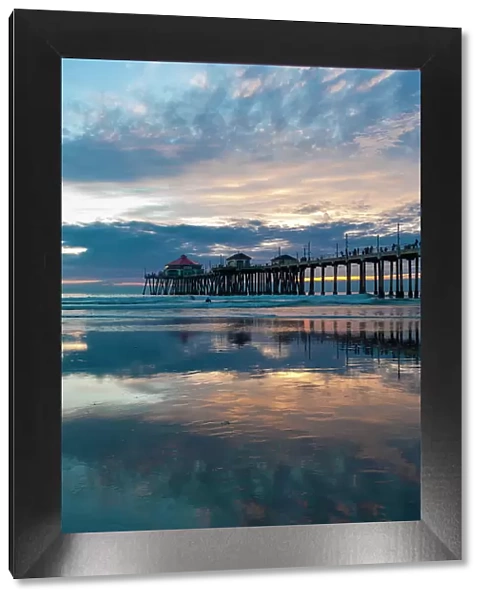 The Huntington Beach Pier and reflections on the wet beach at sunset. Huntington Beach, California