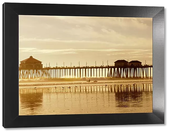 The Huntington Beach Pier and surfers at sunset. Huntington Beach, California