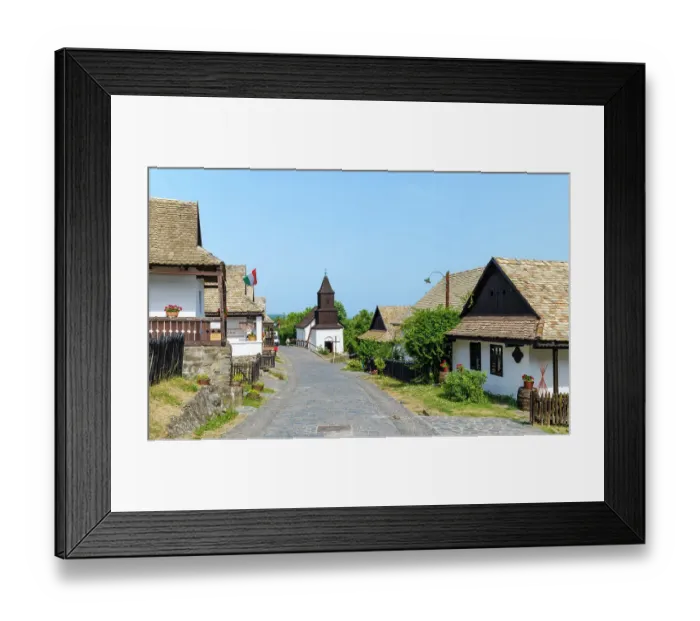 Framed Print : Village high street with church. The Paloc village Holloko in Hungary, listed as UNESCO World Heritage Site. The traditional farm houses form a complete village as it looked during the middle ages Framed Print : Village high street with church. The Paloc village Holloko in Hungary, listed as UNESCO World Heritage Site. The traditional farm houses form a complete village as it looked during the middle ages