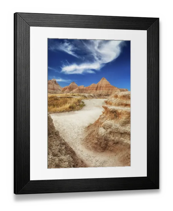 Framed Print : Sandy path leads through the striated peaks to the higher peaks in the background stark against a blue sky
