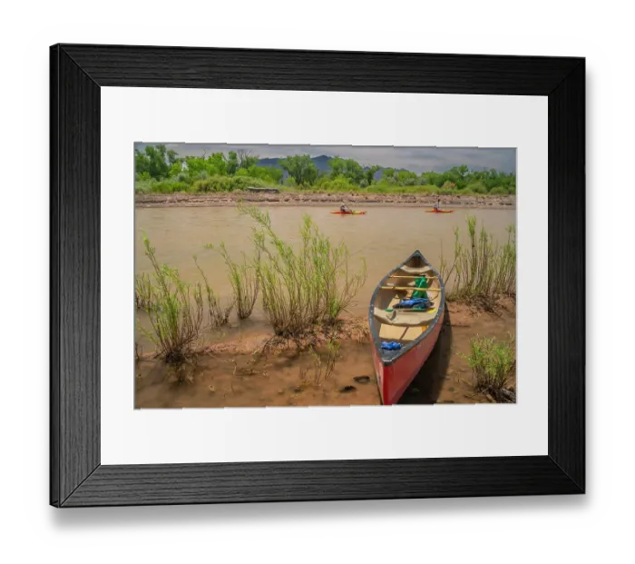 Framed Print : USA, New Mexico, Rio Grande River. Empty canoe on riverbank and kayakers on river