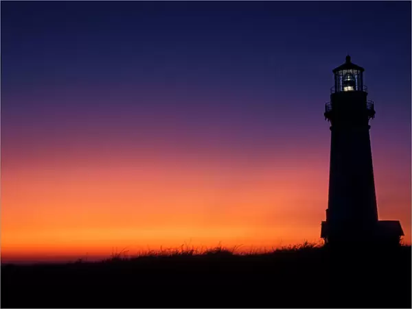 The sun ball drops down on the colorful horizon Yaquina Bay lighthouse on the coast