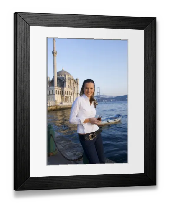 Framed Print : Young woman holding Turkish tea glass, in front of Great Mecidiye Mosque, Ortakoy on the Bosphorus