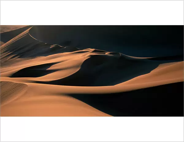 Namibia, Namib Desert, Setting sun lights curving sand dunes near coastal city of