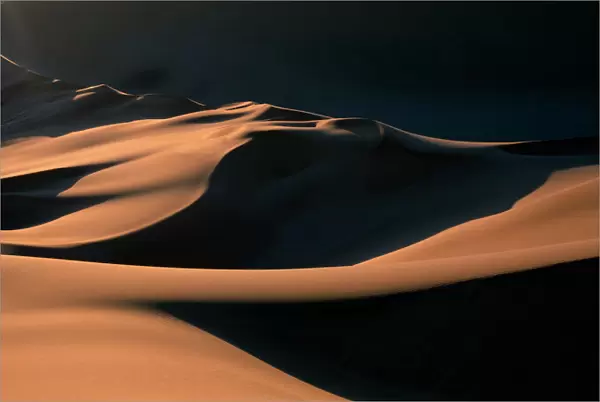 Namibia, Namib Desert, Setting sun lights curving sand dunes near coastal city of