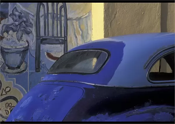 Cuba, Havana. Hand-painted blue car with several hues in front of wall mural