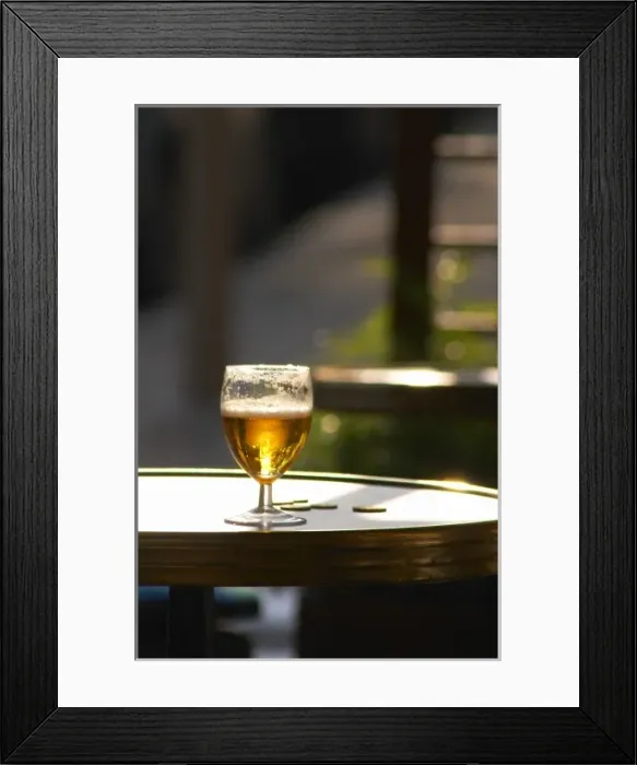 Framed Print : A glass of beer with foam froth with sun backligthing the drink and some change coins