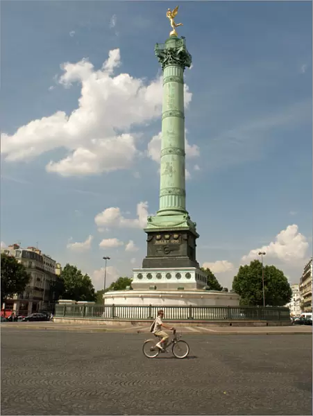 A lone cyclist pedals in front of the Colonne de Julliet at Place de la Bastille, Paris, France