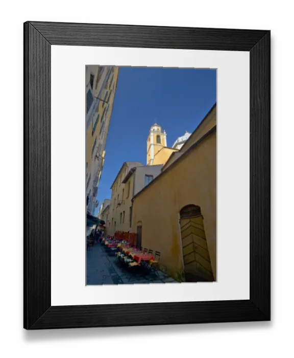 Framed Print : France, Corsica. Church steeple rises above narrow street with tables set up outside Framed Print : France, Corsica. Church steeple rises above narrow street with tables set up outside