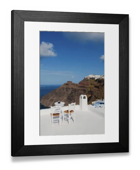 Framed Print : Postcard scene of two lonely chairs on terrace with table ready for tourists in Santorini