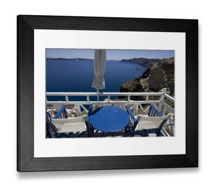 Framed Print : Greece, Santorini. Blue and white patio chairs and table overlooking Aegean Sea