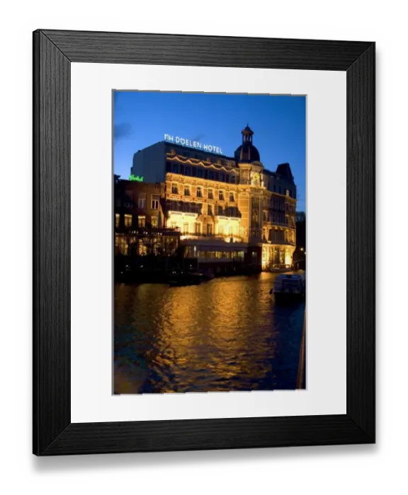 Framed Print : NH Doelen Hotel with lights on at night along the Amstel River in Amsterdam, Netherlands Framed Print : NH Doelen Hotel with lights on at night along the Amstel River in Amsterdam, Netherlands