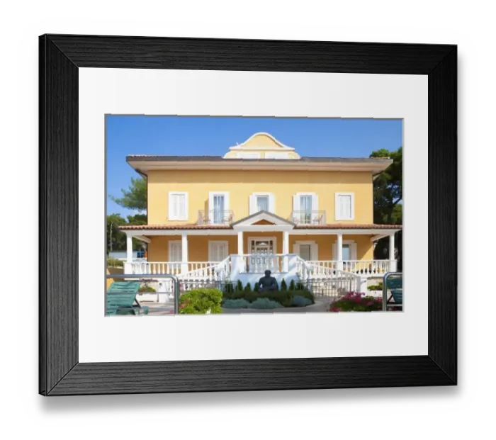 Framed Print : Cres, Coatia - A two level, yellow house with a large porch and well manicured garden