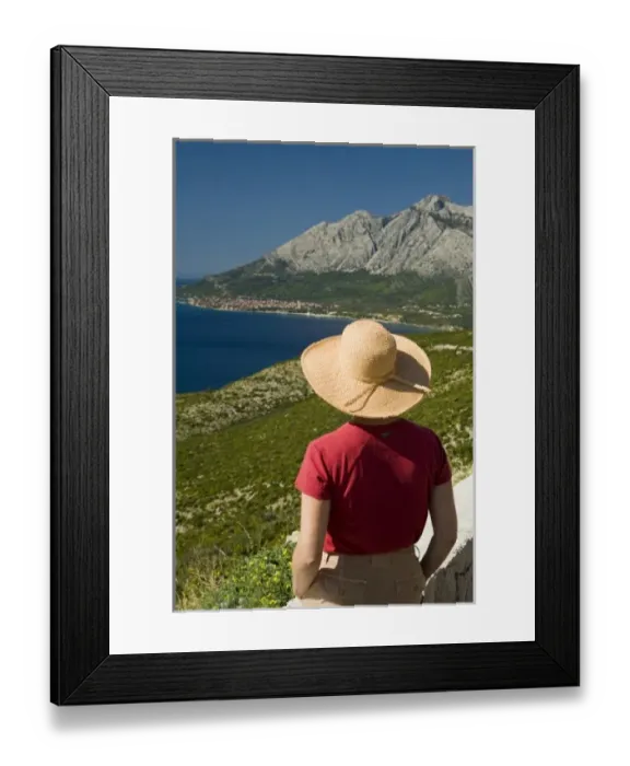 Framed Print : Croatia, Dalmatia, Female tourist in straw hat gazes at lush fields and town of Orebic Framed Print : Croatia, Dalmatia, Female tourist in straw hat gazes at lush fields and town of Orebic