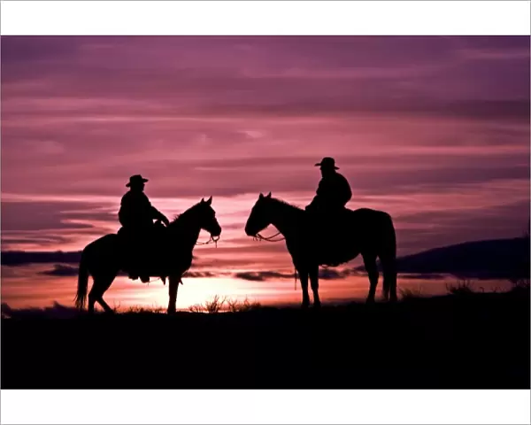 A silhouette of two cowboys on horses with the winter sky on The Hideout Ranch in Shell Wyoming
