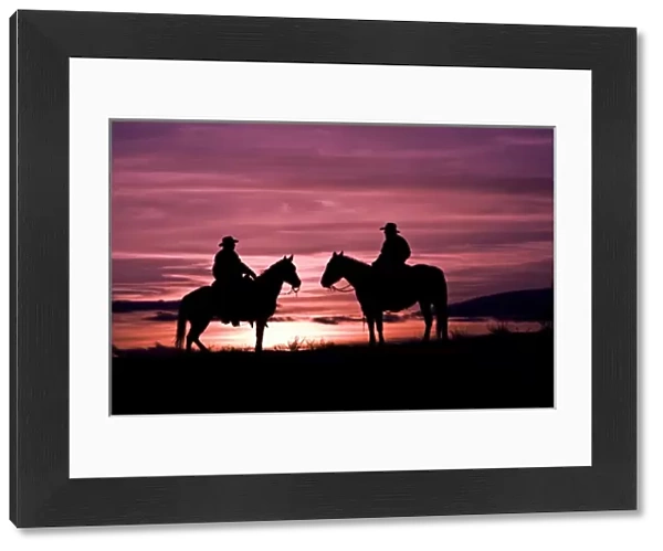 A silhouette of two cowboys on horses with the winter sky on The Hideout Ranch in Shell Wyoming