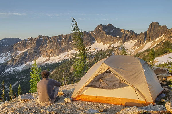 Adult man at daybreak sitting next to backpacking tent and gazing at view of Cutthroat