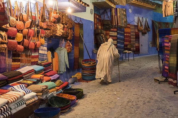 Africa, Morocco. An elderly man walks past tourist shops along a street in the blue