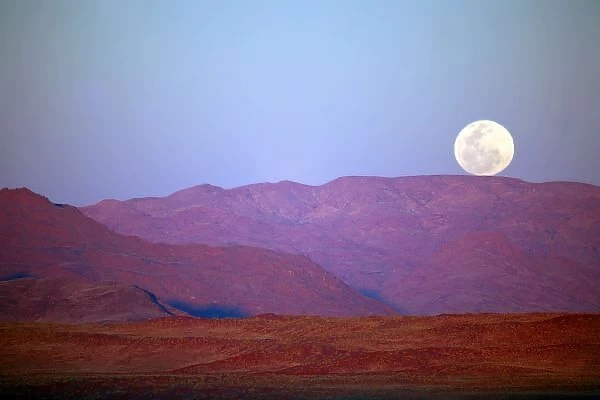 Africa, Namibia, Sossusvlei. A full moon rests on the crest of foothills in the NamibRand